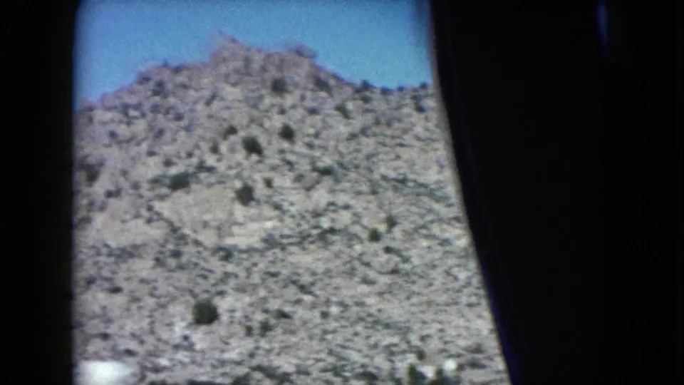 A rocky Nevada desert slope fills the frame, with sparse scrub and dark car-window framing at the edge.