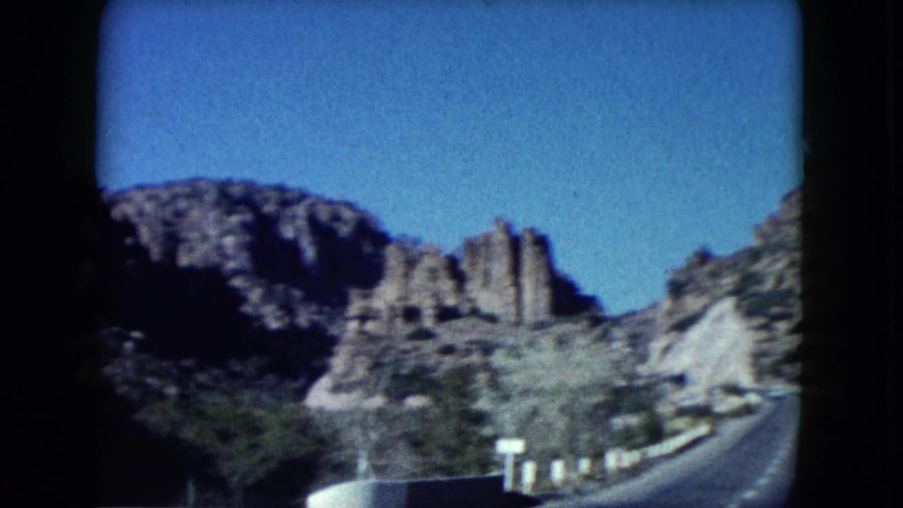 1960 Nevada home-movie frame showing a curving highway through rocky desert terrain with rounded 8mm frame edges.