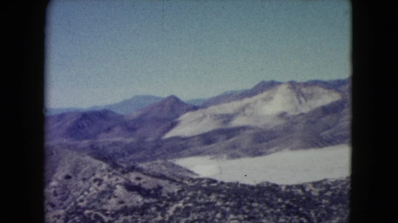 Distant desert mountains and pale slopes beyond scrub-covered foreground hills.