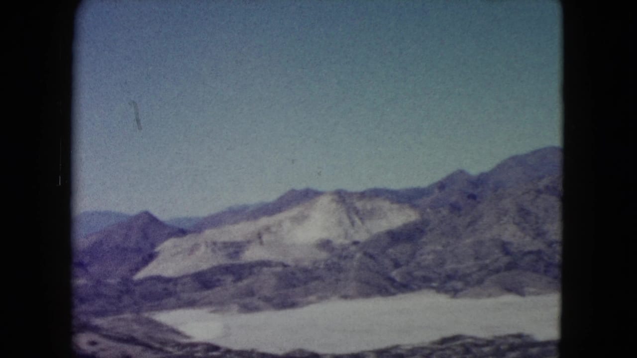 1960 Nevada 8mm view of a rugged mountain ridge, pale exposed slopes, and open desert terrain seen from a high vantage point.
