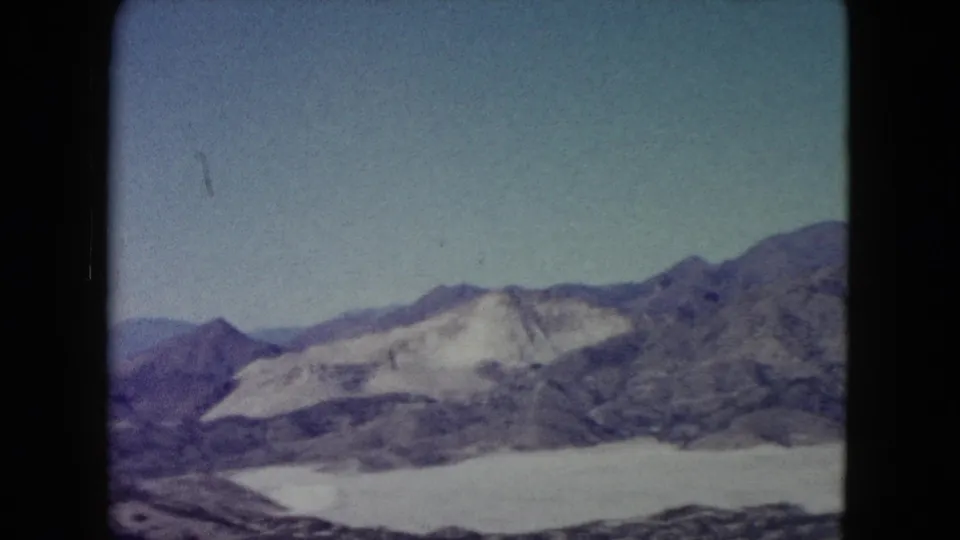 1960 Nevada 8mm view of a rugged mountain ridge, pale exposed slopes, and open desert terrain seen from a high vantage point.