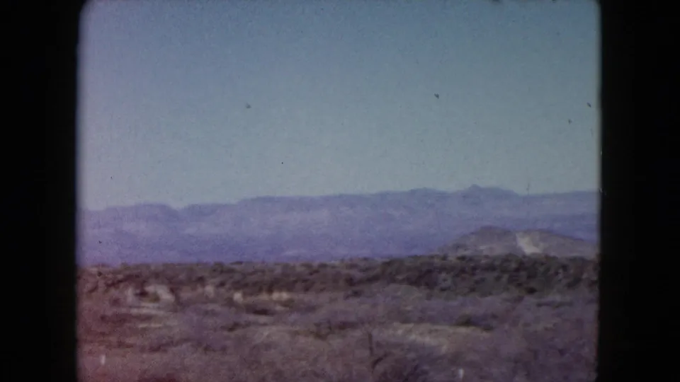 1960 Nevada 8mm frame showing scrubby open desert, low rolling hills, and a hazy mountain range across the horizon.