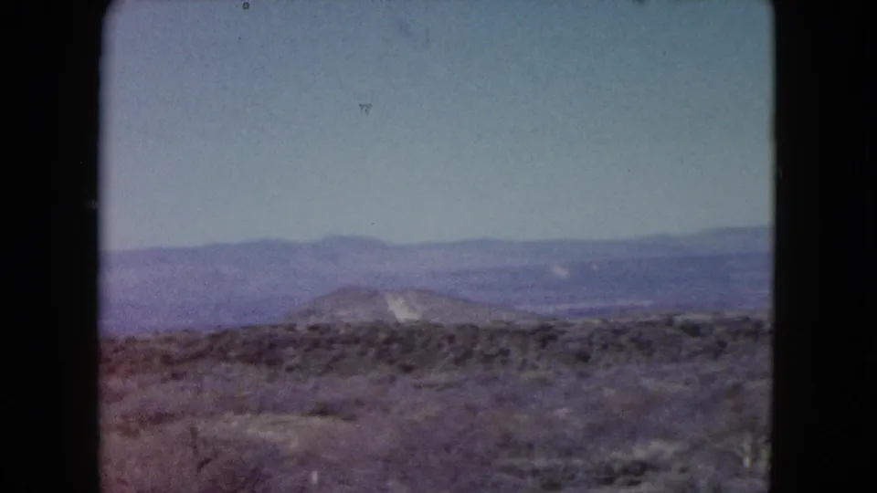 1960 Nevada 8mm view across scrubland toward a rounded hill and distant mountain range, with faded color and soft home-movie texture.