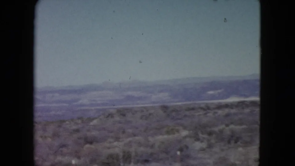 1960 Nevada 8mm landscape frame with desert brush in the foreground and layered ridgelines fading into haze.