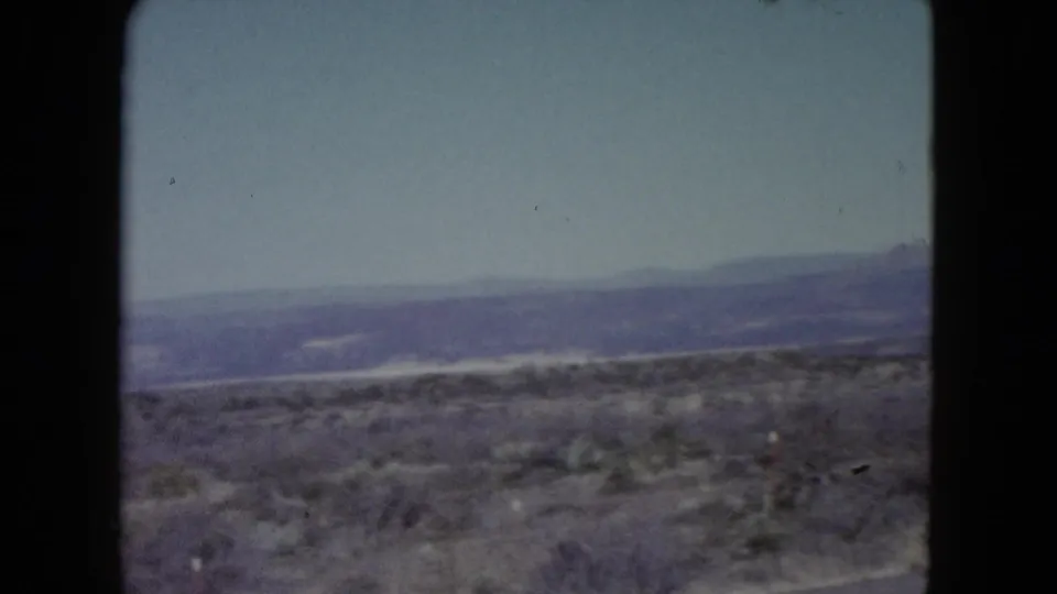 1960 Nevada 8mm frame showing scrub-covered terrain, a broad hazy mountain range, and soft faded color.