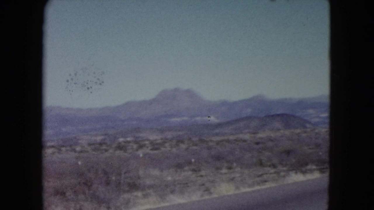 1960 Nevada desert landscape with sparse shrubs, a low hill, and hazy mountain forms in the distance.