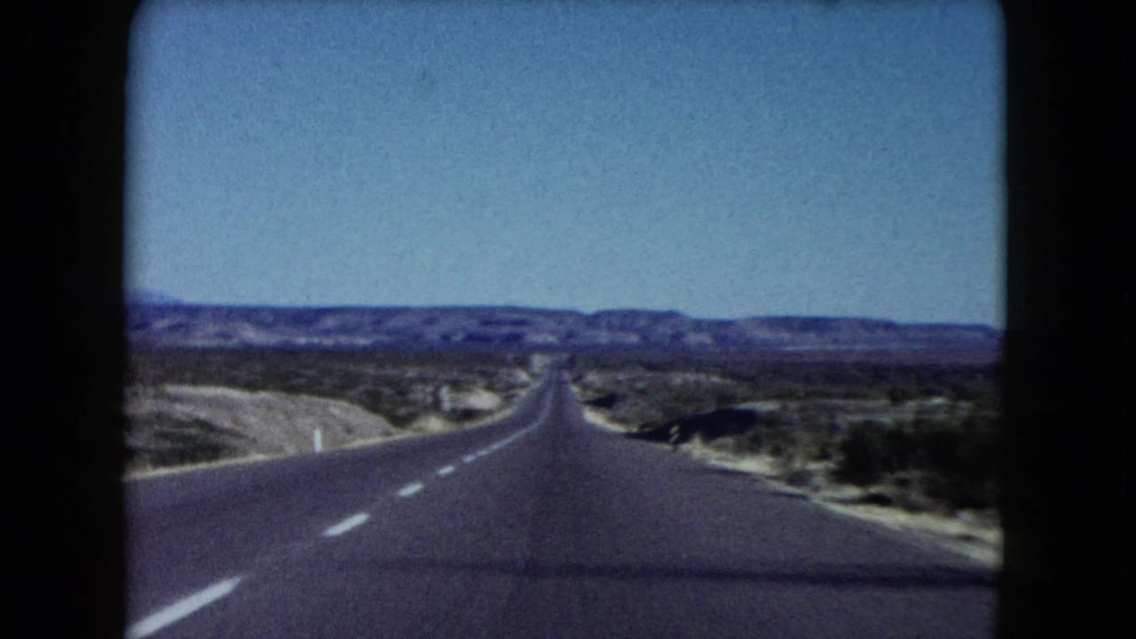 Empty paved road running through arid scrubland toward distant mountains.