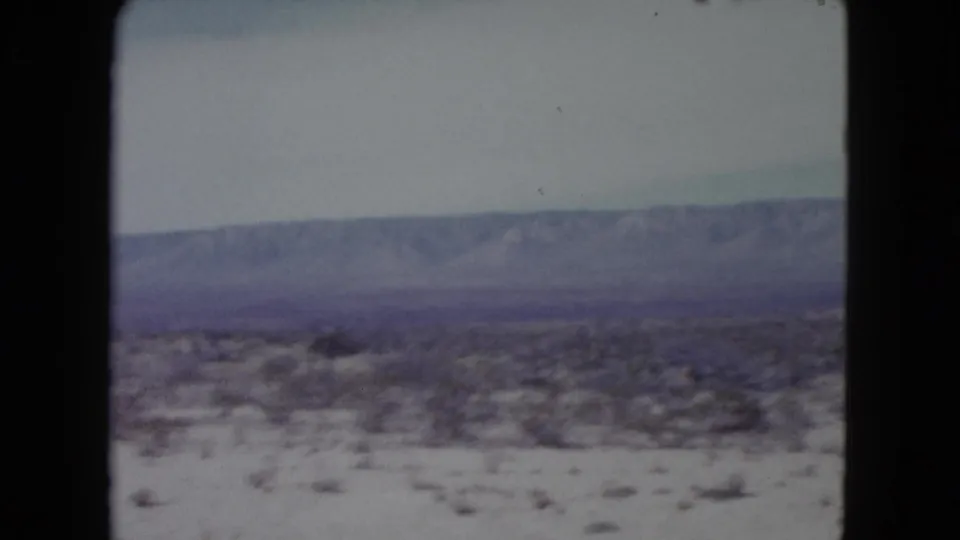 Nevada desert landscape on 8mm film, with scrub vegetation, open ground, and a broad distant ridge.