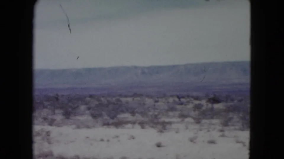 1960 Nevada home-movie frame of a dry bushy landscape below a hazy mountain range.