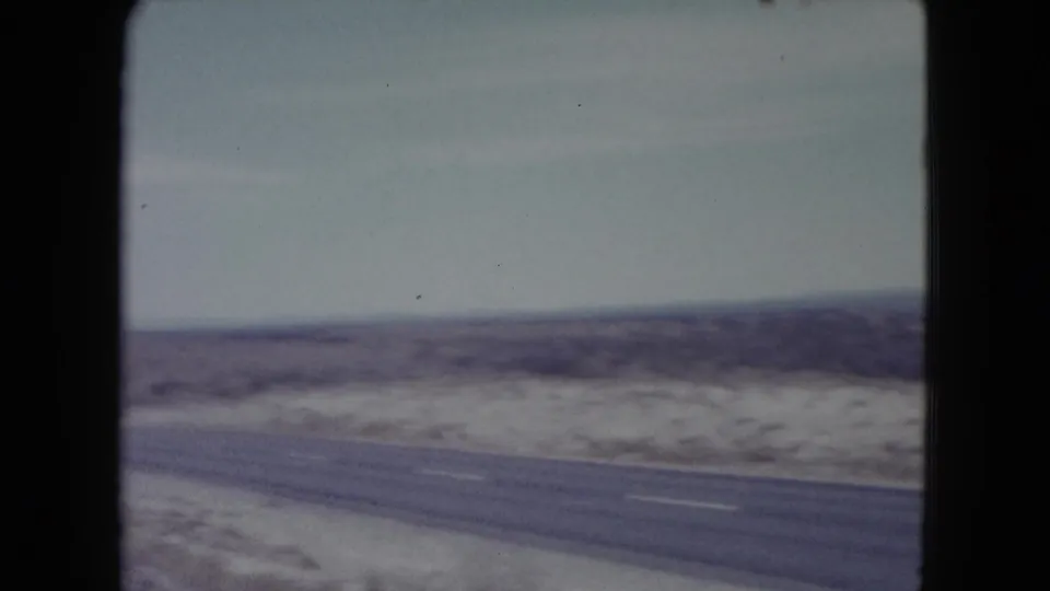 1960 Nevada 8mm frame of a quiet paved desert road running through open scrubland toward low distant hills.