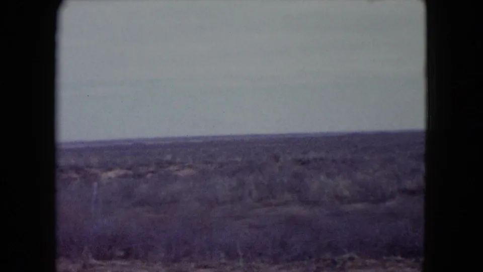 1960 Nevada 8mm frame of open arid land with scrub vegetation, a low horizon, and washed pale sky.