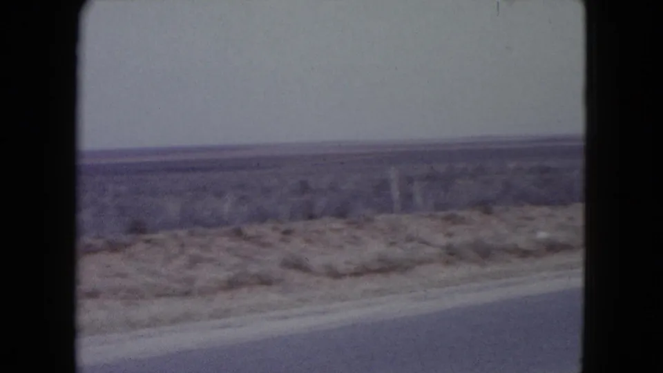 1960 Nevada 8mm frame with motion-softened roadside scrub, a paved shoulder, and flat desert horizon.