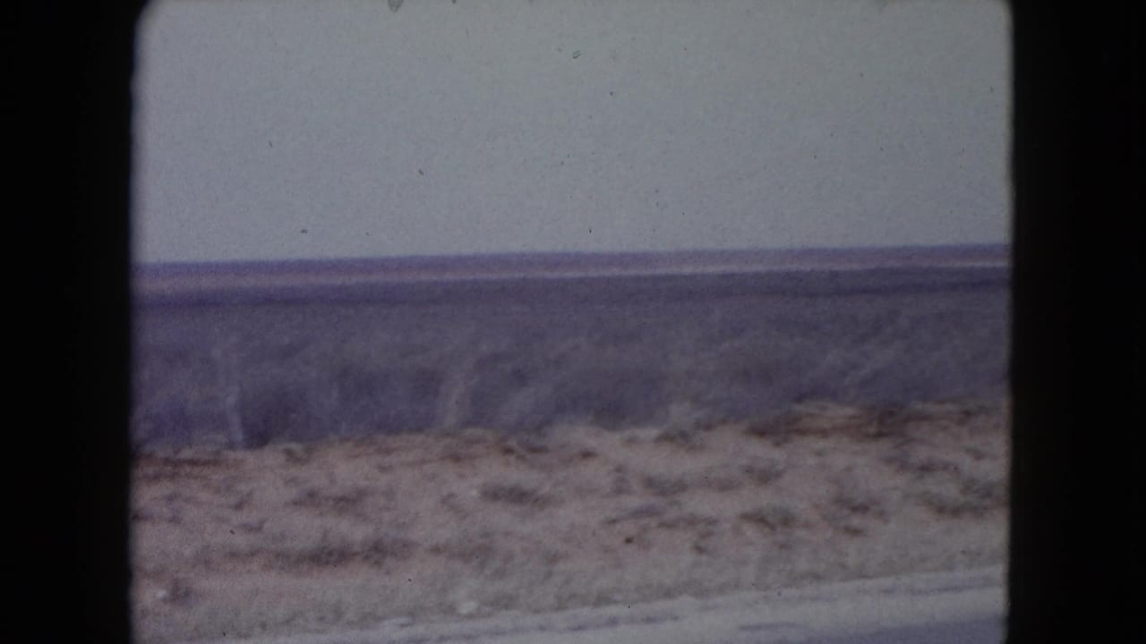 Dry desert scrubland and pale sky seen through dark 8mm frame borders.