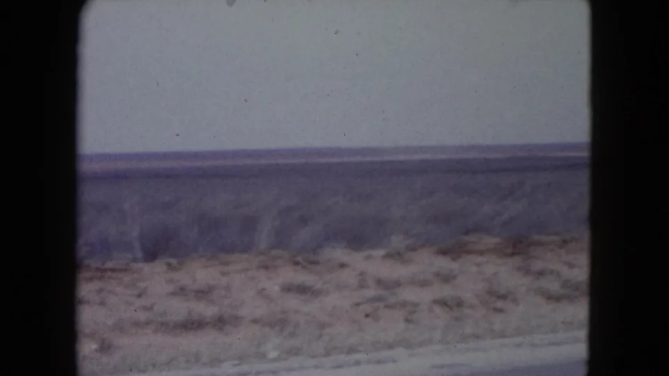 1960 Nevada 8mm home-movie frame showing flat dry desert scrubland beside a road under a pale sky.