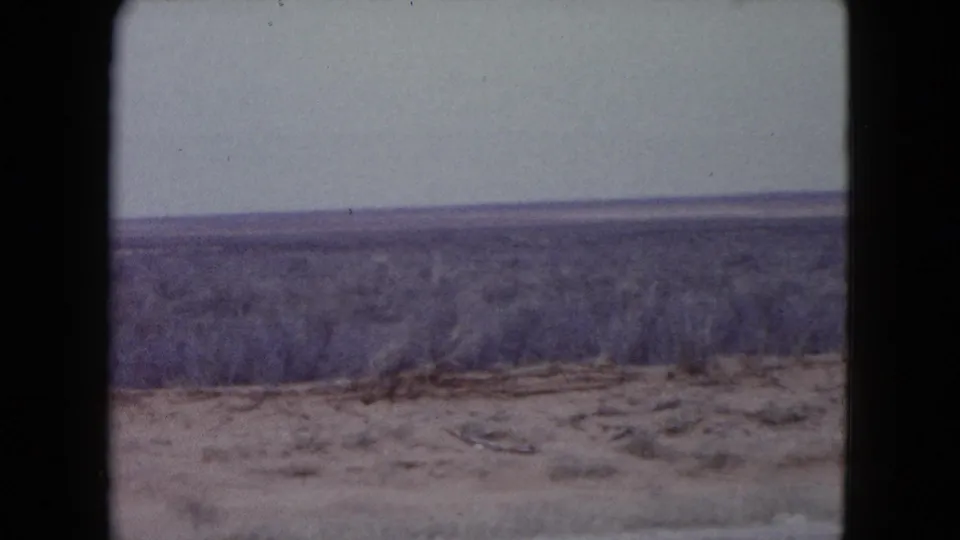 Faded 8mm view of Nevada scrub desert from the side of a road, with no people or structures visible.