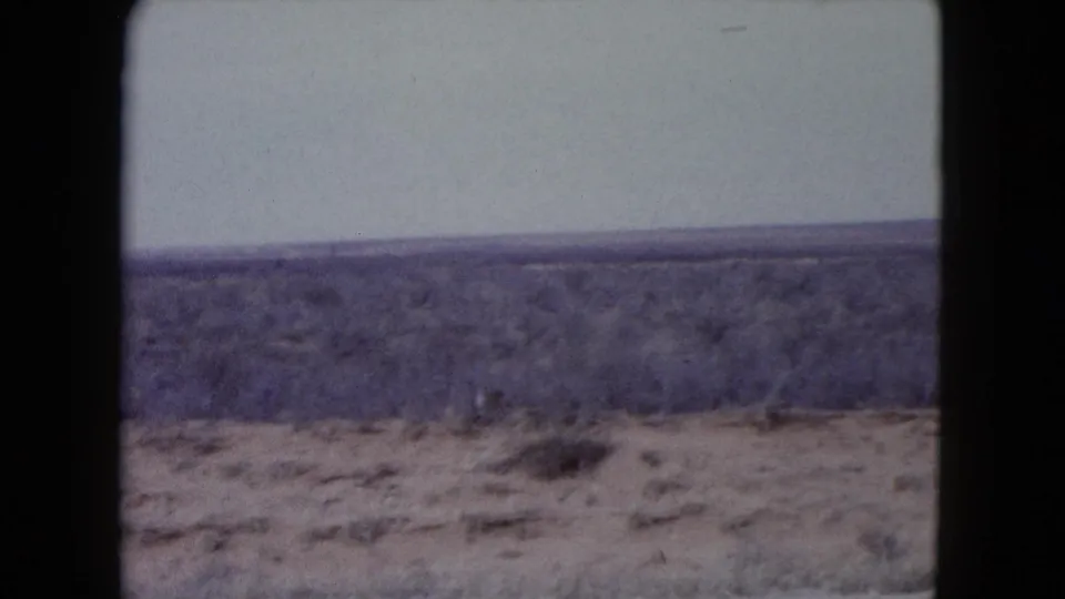 1960 home-movie frame of arid Nevada scrubland and a low horizon, bordered by the scanned 8mm film gate.