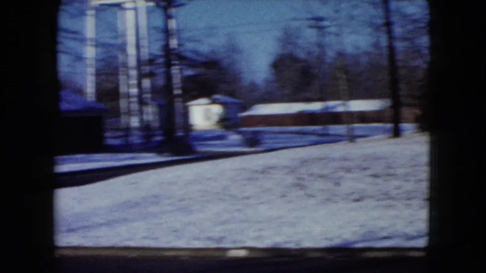 Snowy neighborhood scene with bare trees, utility poles and distant houses, suggesting a winter holiday travel stop.