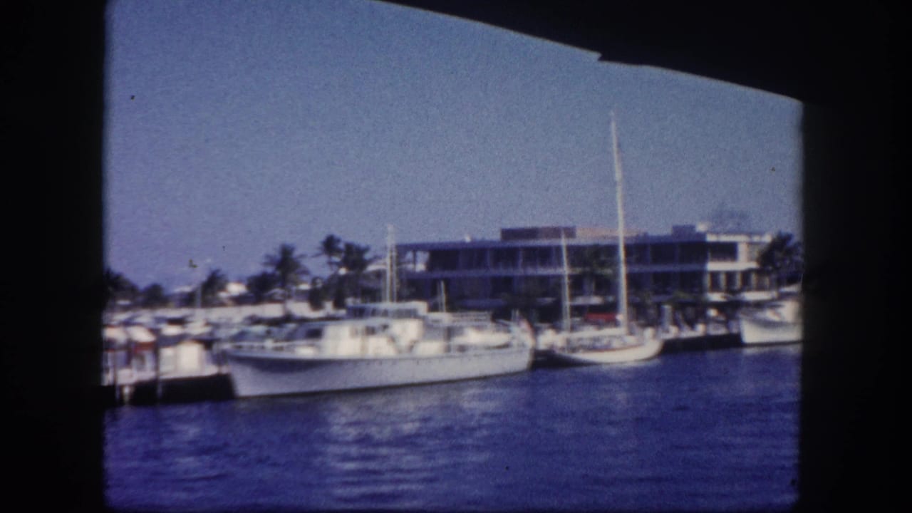 White boats docked beside a waterfront building seen across blue channel water.