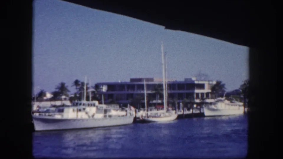 1960 Tampa waterfront view with several boats moored near a low modern building, framed by dark film edges.