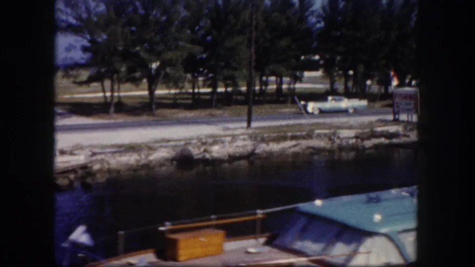 Tampa marina channel with a moored boat in the foreground and classic cars passing or parked beyond the water.
