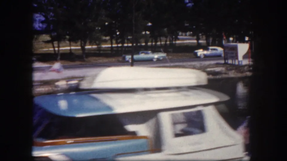 Light blue and white motorboat in a Tampa marina, with classic cars and trees visible across the channel.