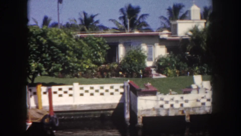 1960 Tampa-area waterfront residence seen from the water, with palms, lawn, shrubs, and a patterned seawall.