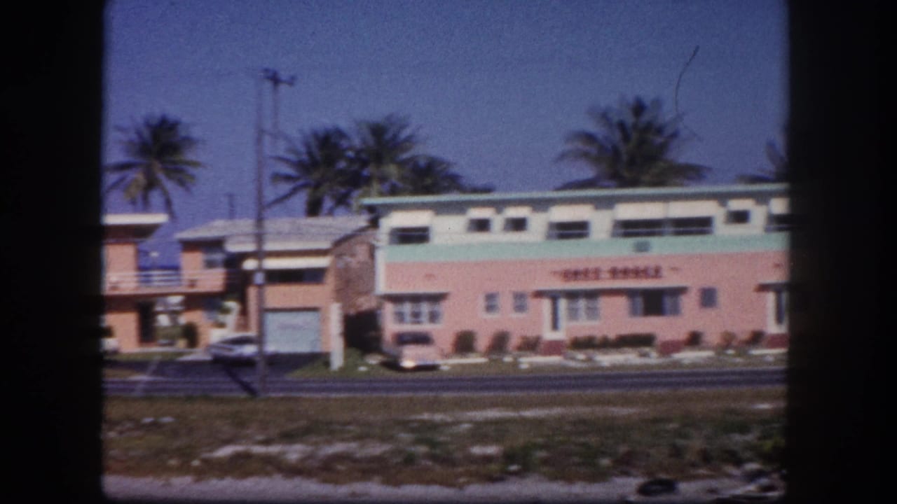 Pastel roadside motel seen from across a street with palm trees behind it.
