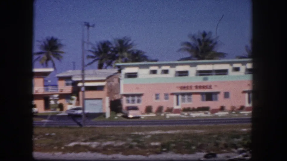 1960 Tampa street view of a pastel low-rise motel, palm trees, utility poles, and a road in the foreground.