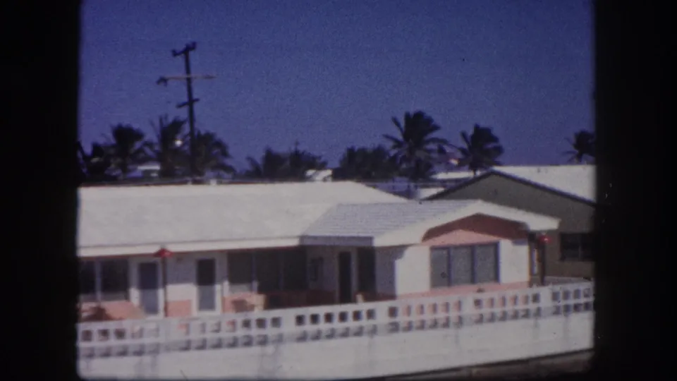 1960 Tampa home-movie view of a single-story residence with pink accents, a low fence, palms, and visible overhead utility lines.