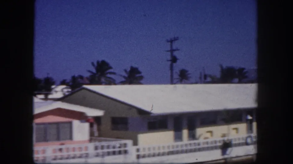 1960 Tampa frame showing a yellow-toned single-story home behind a low fence, with palms, blue sky, and a utility pole.