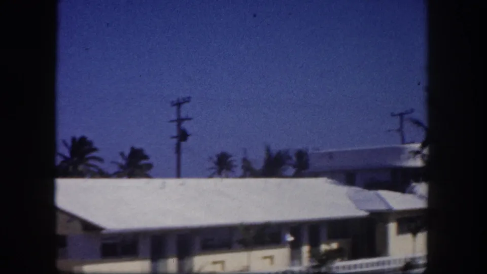 1960 Tampa home-movie frame showing a white waterfront building, palms, utility pole, and canal-side architecture through dark frame edges.