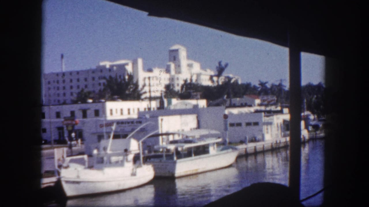 Docked boats beside white waterfront buildings viewed from a shaded opening.