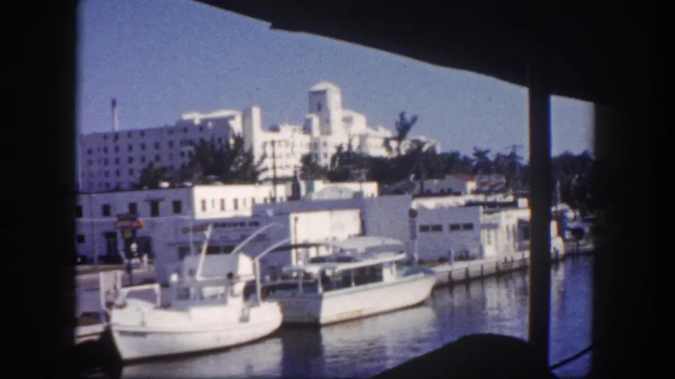 1960 Tampa waterfront view with small boats, white buildings, palm trees, and dark window-like framing in the foreground.