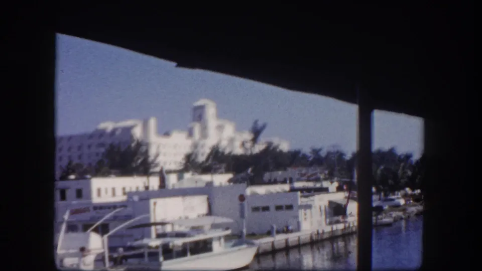 1960 Tampa shoreline with white buildings, palms, and boats, partially obscured by shaded posts or cabin framing.