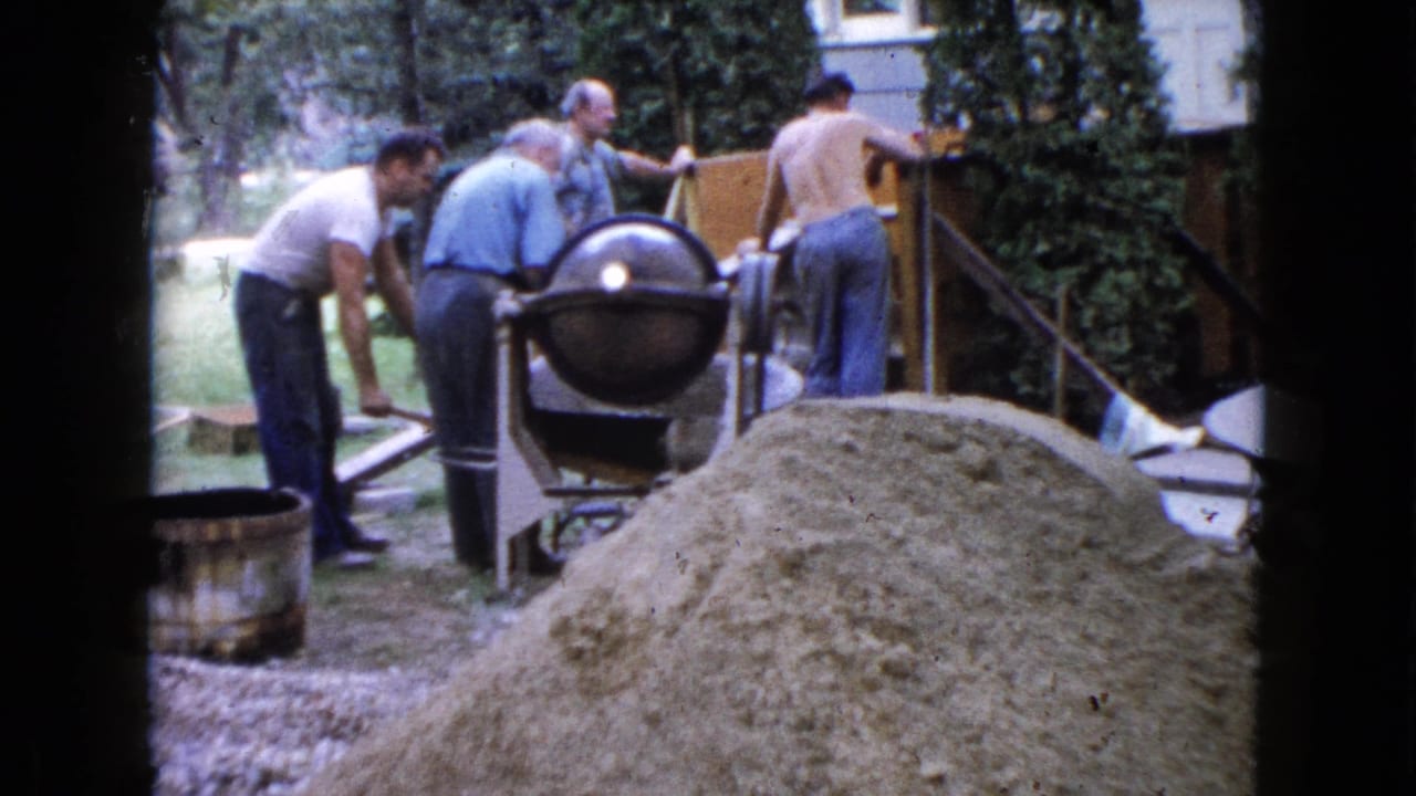 Four men work near a cement mixer and sand pile in a backyard.