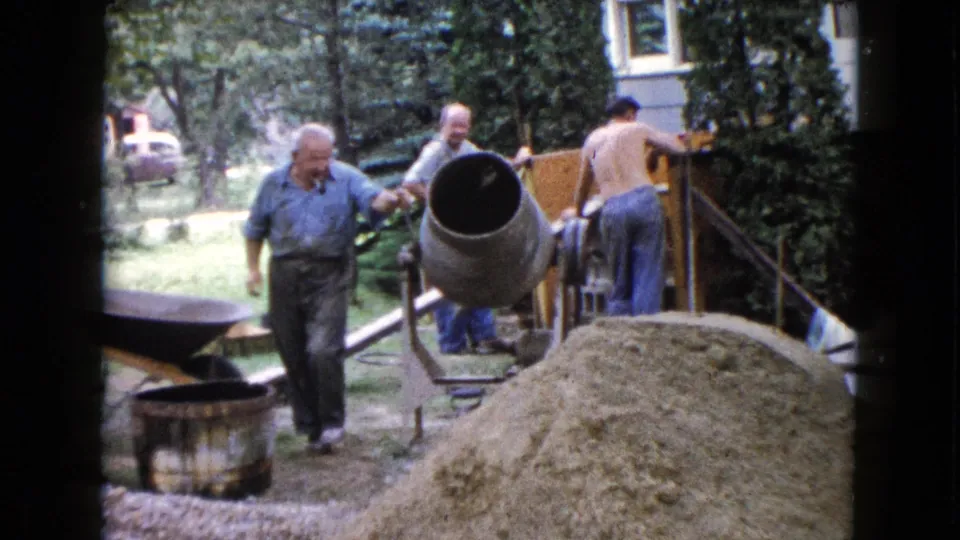 The cement mixer is tilted toward the camera as men continue working near a sand pile and house steps in the Wauconda yard.