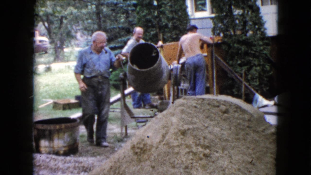 Men working around a cement mixer and sand pile beside a backyard porch structure.