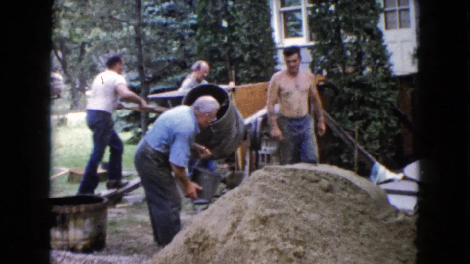 1960 Wauconda, Illinois backyard scene with men working near a cement mixer, sand pile, and porch structure during concrete preparation.