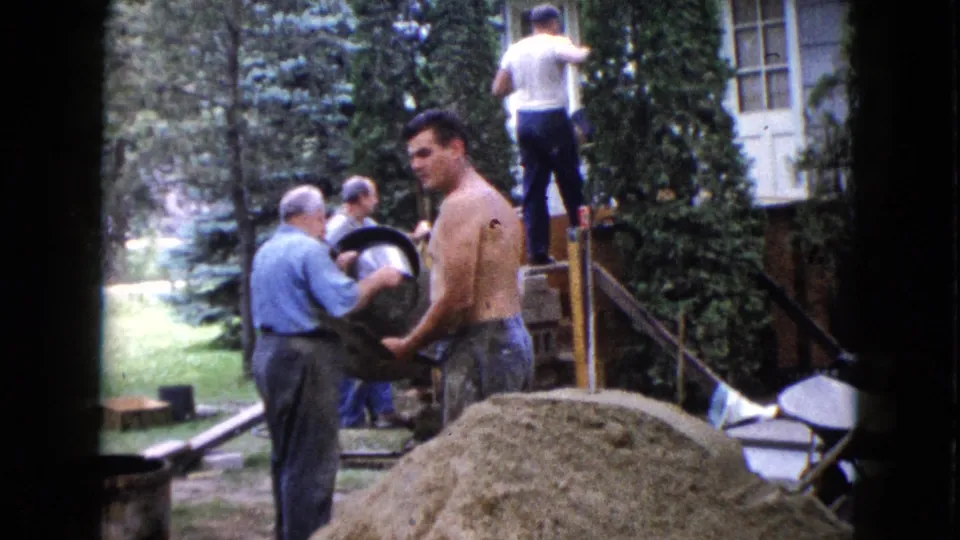 A shirtless adult man holds a large bucket in a Wauconda yard as other men work near exterior steps and a ladder.