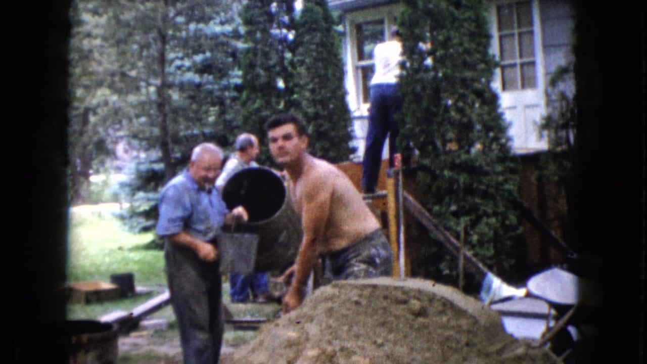 Men work beside a cement mixer and sand pile outside a house.