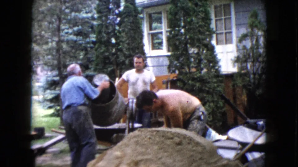 1960 Wauconda frame showing an older man handling a cement mixer while men work around a backyard sand pile.