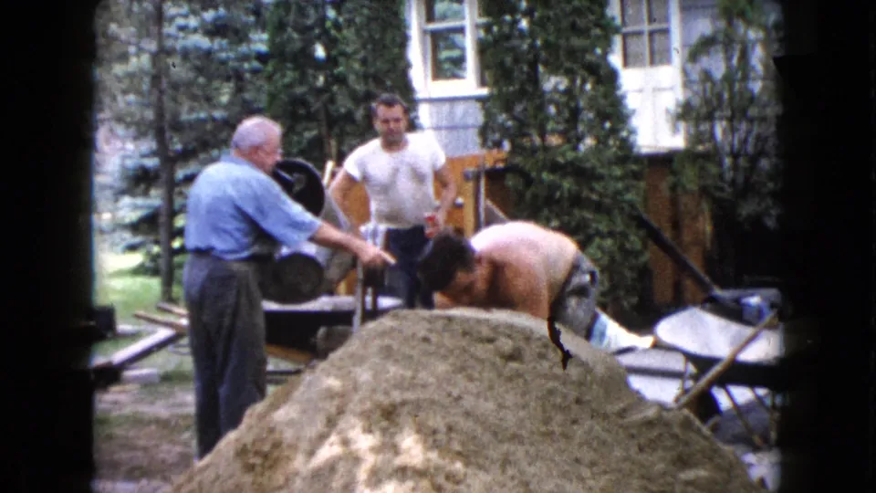 1960 Wauconda backyard construction frame with men working around a cement mixer, sand pile, and house steps.