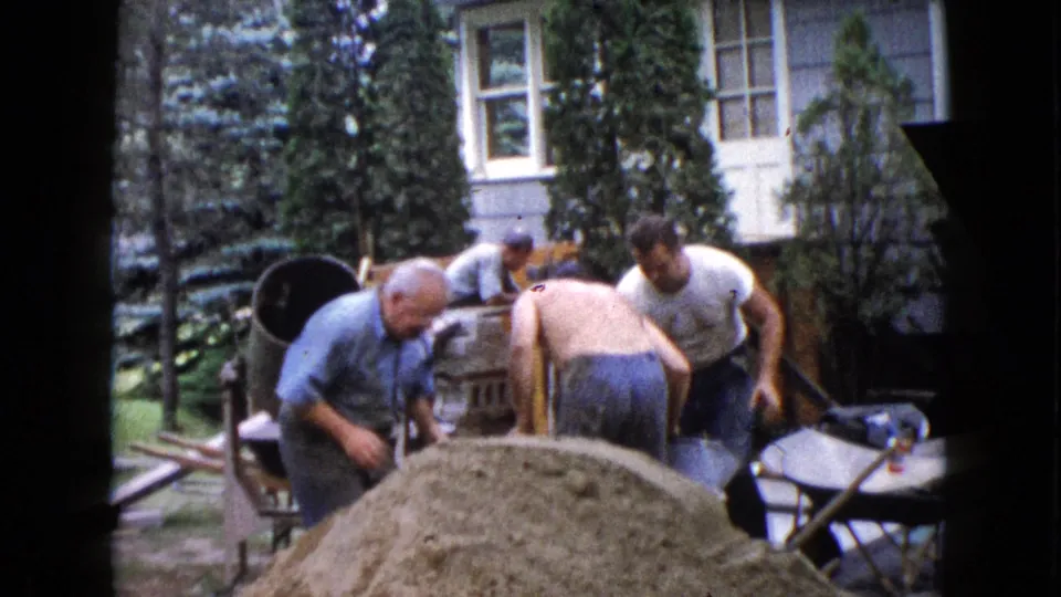 The final frame shows adult men in a 1960 Wauconda backyard working around a sand pile, mixer, wheelbarrow, and residential exterior.