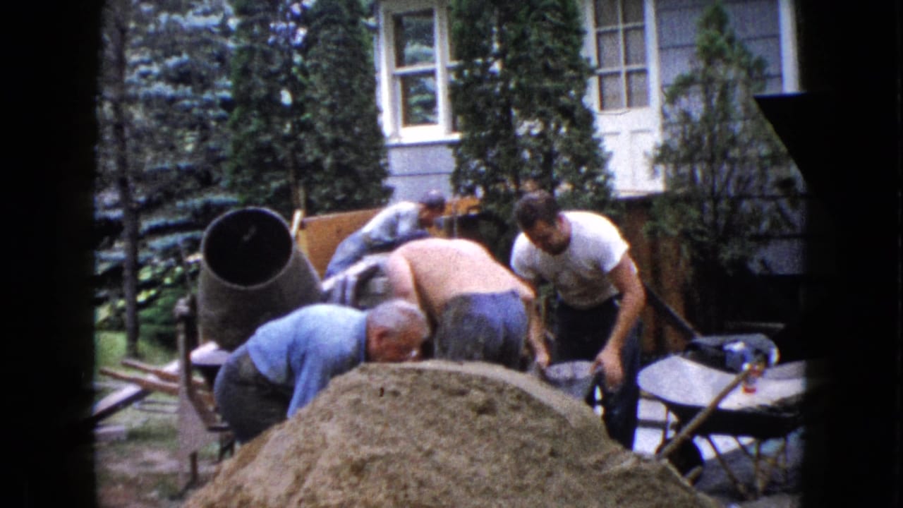 Adult men work beside a cement mixer and sand pile in a backyard.