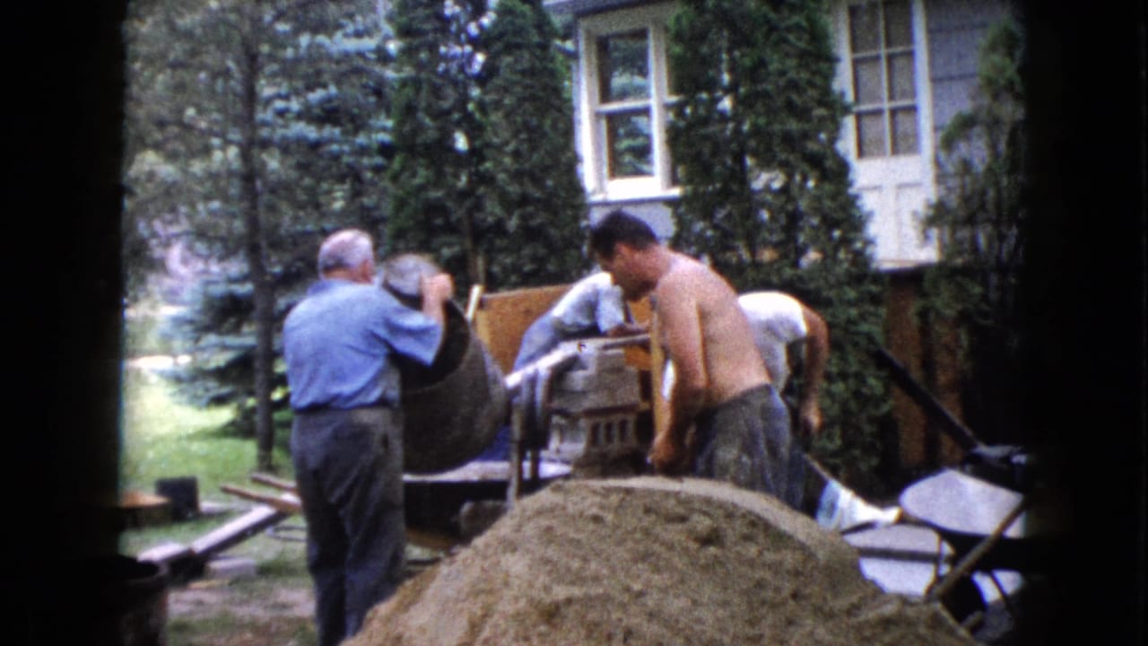 1960 Wauconda backyard construction scene with a shirtless man and others positioned around a cement mixer and work materials.
