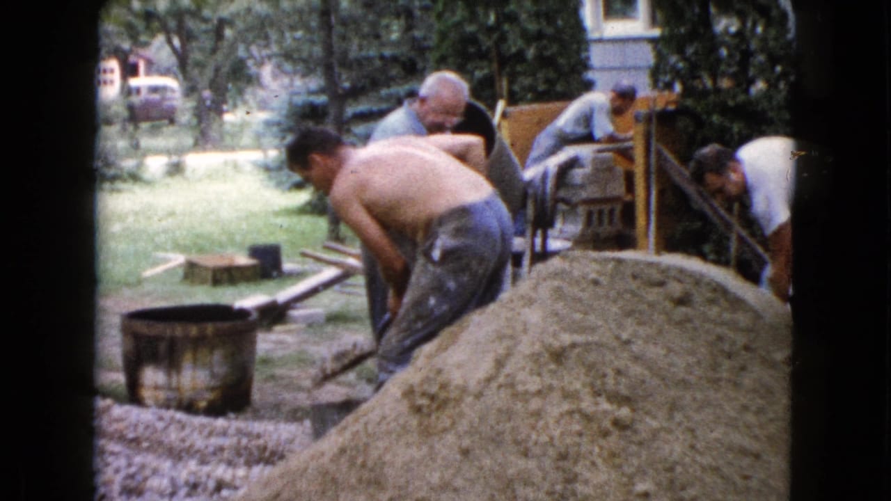 Men work around gravel and sand piles beside a small cement mixer in a backyard.