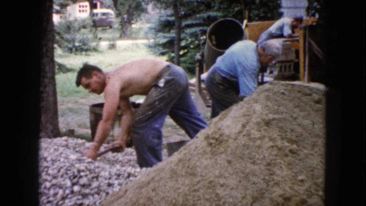 In this 1960 Wauconda backyard scene, a man shovels gravel as others handle materials near a cement mixer.