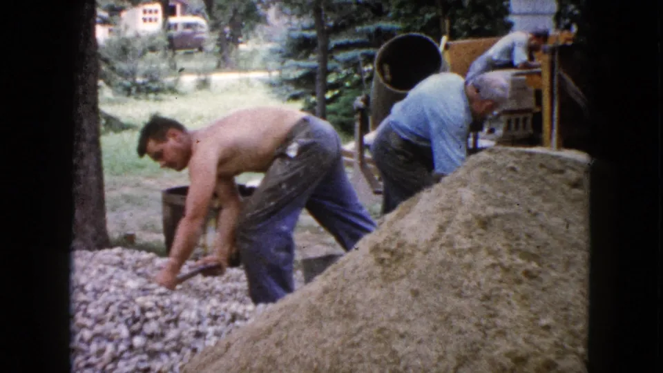 In this 1960 Wauconda backyard scene, a man shovels gravel as others handle materials near a cement mixer.