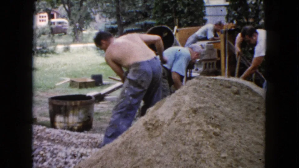 Adult men work beside a sand pile and cement mixer during a 1960 Wauconda backyard construction scene.