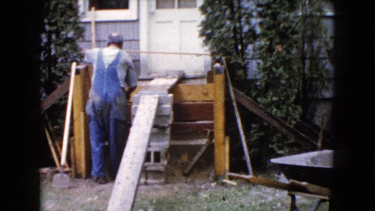 The man stands with his back to the camera beside a wooden ramp and concrete blocks during a 1960 backyard porch project in Wauconda.